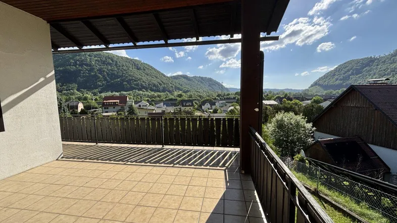 Geräumige Terrasse mit Fliesenboden und weitem Blick auf die umliegende Berglandschaft unter blauem Himmel.