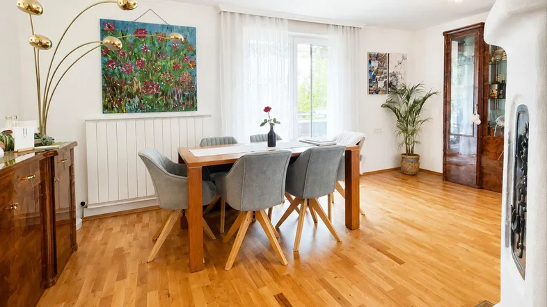 Heller Essbereich mit Holzboden, großem Esstisch und einem traditionellen Kachelofen.