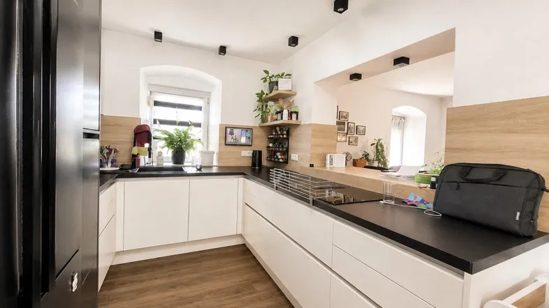 Moderne Küche mit weißen Schränken, dunklen Arbeitsplatten und Holzakzenten, offen zum Wohnbereich.