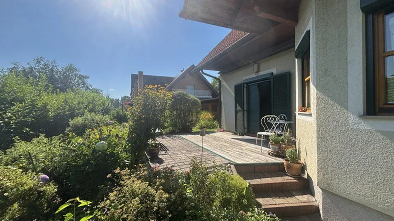 Sonnige Terrasse mit Gartenmöbeln, umgeben von üppigem Grün und Pflanzen.