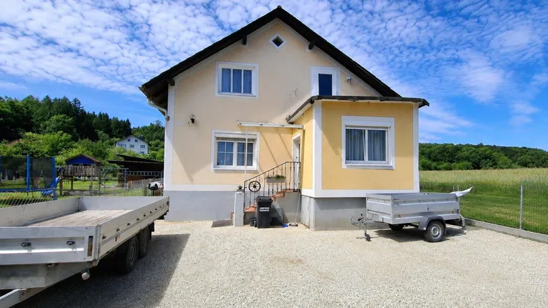 Einfamilienhaus mit heller Fassade, großem Vorplatz und ländlicher Umgebung unter blauem Himmel.