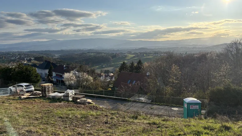 Weitläufige Landschaft mit Bergblick und Baugrundstück im Vordergrund bei Sonnenuntergang.