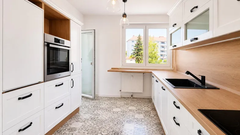 Helle Küche mit weißen Schränken, Holz-Arbeitsplatten und gemustertem Fliesenboden, inklusive Backofen und Kochfeld.