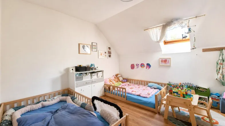 Helles Kinderzimmer mit zwei Betten, Holzboden und Dachfenster unter der Dachschräge.