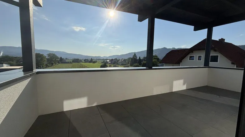 Große Sonnenterrasse mit moderner Pergola, Fliesenboden und weitem Blick auf Berge und grüne Landschaft.