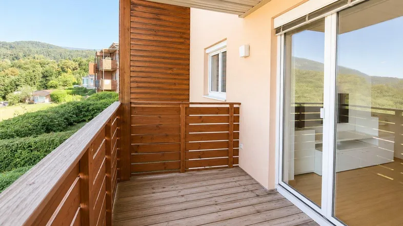 Heller Balkon mit Holzboden und Holzgeländer, bietet einen weiten Blick auf die grüne Landschaft.