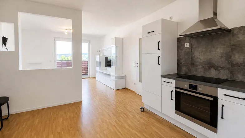 Heller offener Wohnbereich mit integrierter Küche, Parkettboden und Zugang zum Balkon.