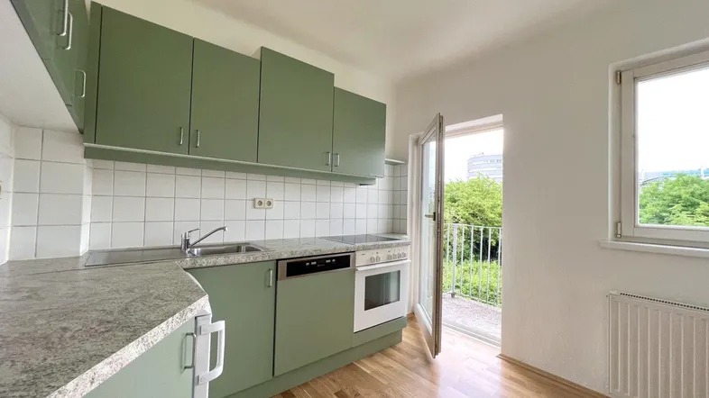 Grüne Einbauküche mit Granitarbeitsplatte, Holzboden und Zugang zu einem kleinen Balkon.
