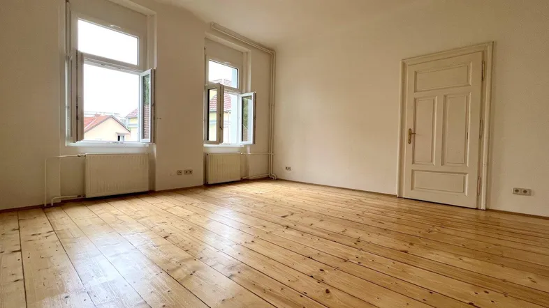 Helles Zimmer mit Holzdielenboden und großen Fenstern, die viel Tageslicht hereinlassen.