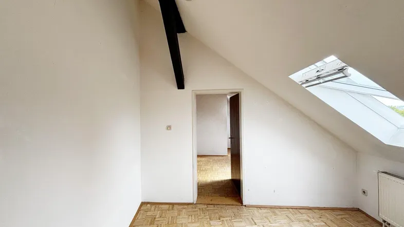 Heller Raum im Dachgeschoss mit Schrägdach, Parkettboden und Dachfenster, ideal für flexible Nutzung.