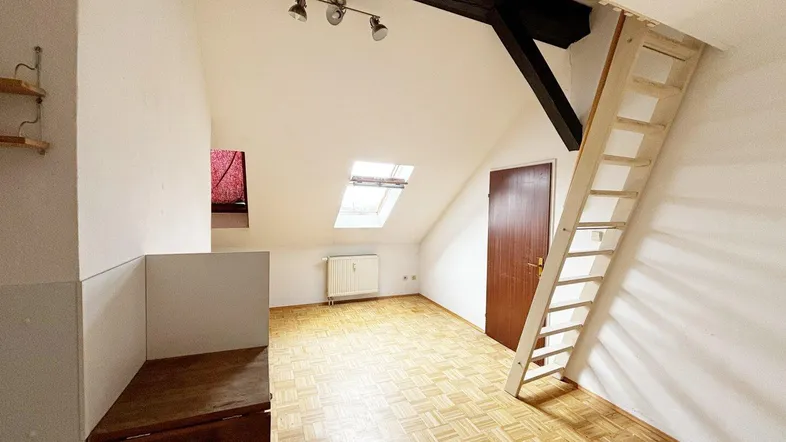 Heller Dachbodenraum mit schrägen Wänden, Dachfenster und einer Holzleiter zu einer oberen Ebene.