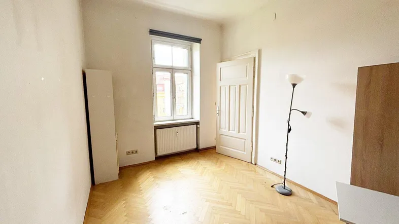 Leerer Raum mit Fischgrätparkett, Fenster und Heizkörper, bereit zur individuellen Gestaltung.