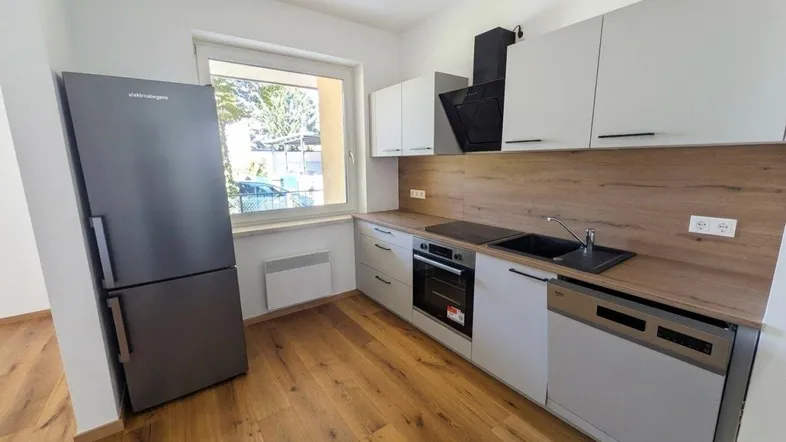 Moderne Küche mit hellgrauen Schränken, Holzarbeitsplatte, integrierten Geräten und Fenster.
