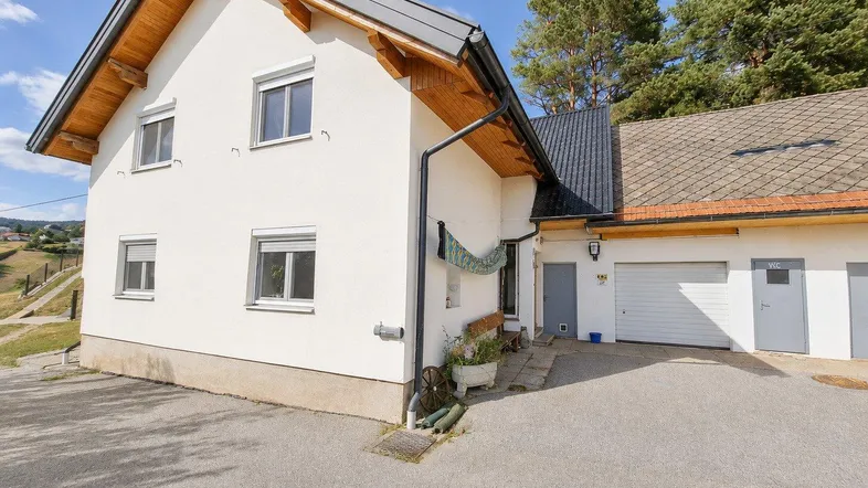Weißes Wohnhaus mit Holzelementen, Satteldach und angrenzender Garage in ländlicher Umgebung.