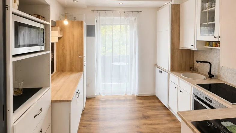 Helle Küche mit weißen Schränken, Holzarbeitsplatten, integrierten Geräten und Zugang zum Balkon.