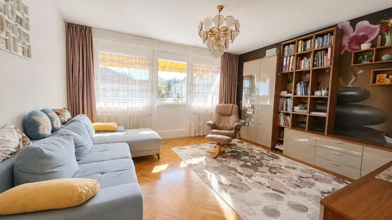 Helles Wohnzimmer mit Parkettboden, bequemer Couch und einem großen Bücherregal.