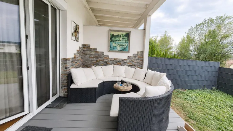 Gemütliche überdachte Terrasse mit bequemer Sitzgruppe, Holzdeck und dekorativer Steinwand.