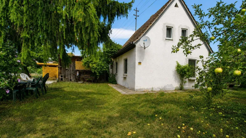 Weißes Einfamilienhaus mit großem Garten, alten Bäumen und einer gemütlichen Sitzecke im Freien.