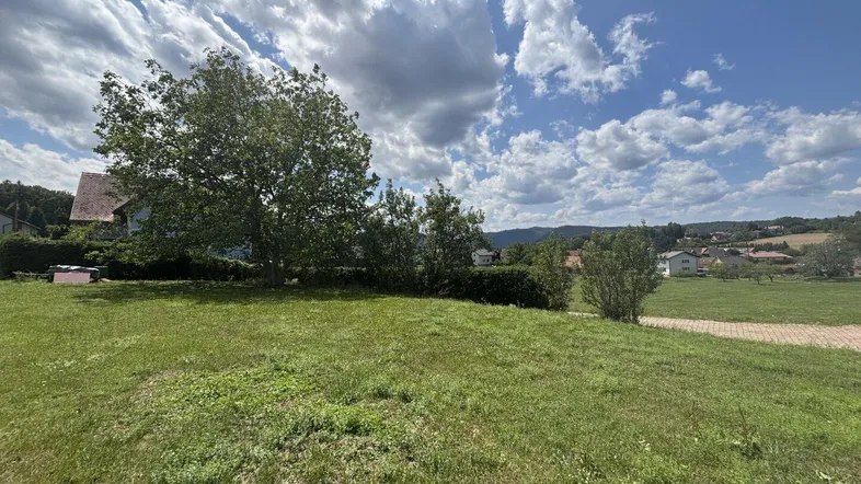 Weitläufige Grünfläche mit Blick auf die umliegende Landschaft und Häuser in der Ferne unter bewölktem Himmel.