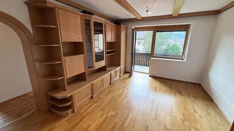 Helles Wohnzimmer mit Holzbalkendecke, Parkettboden und Zugang zu einem kleinen Balkon.