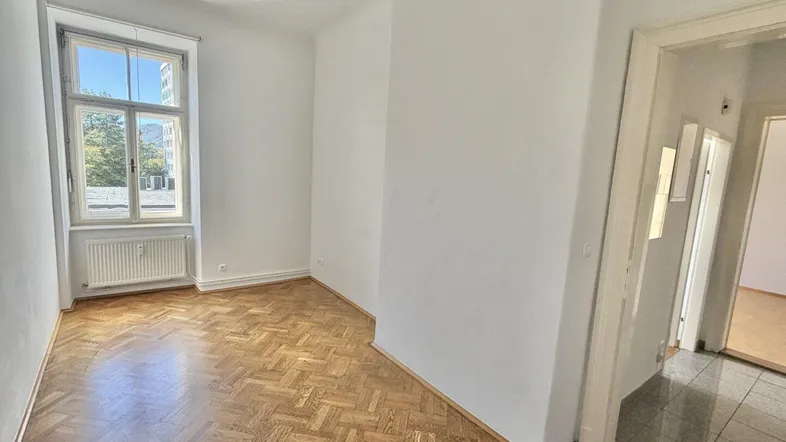 Helles Zimmer mit Fischgrätparkettboden und großem Fenster, ideal als Wohn- oder Schlafzimmer.