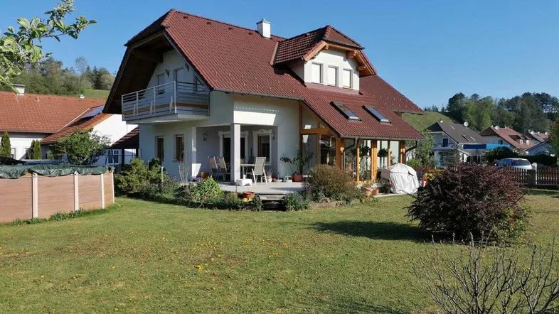 Freistehendes Einfamilienhaus mit Garten, Terrasse und Balkon unter blauem Himmel.