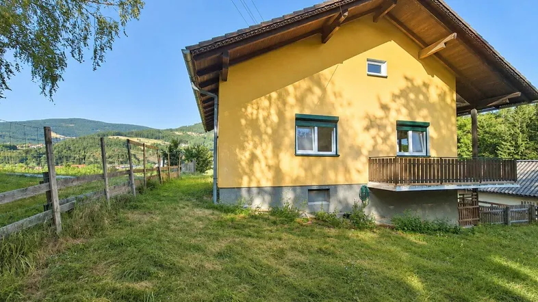 Gelbes Haus mit Satteldach und grünen Fensterläden, umgeben von ländlicher Natur und Hügeln.