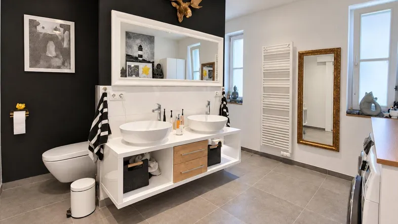 Modernes Badezimmer mit Doppelwaschbecken, Wand-WC, Handtuchheizkörper und Fliesenboden.