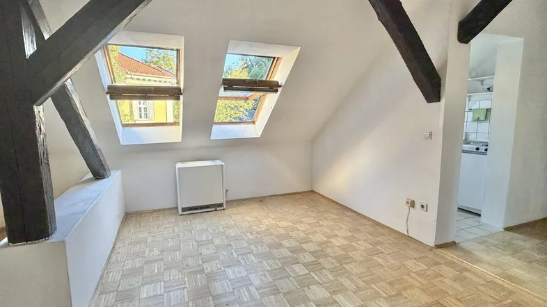 Helles Dachgeschosszimmer mit sichtbaren Holzbalken, Parkettboden und zwei Dachfenstern.