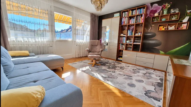 Helles Wohnzimmer mit Fischgrätparkett, großem Fenster und Bücherregal, das viel Stauraum bietet.