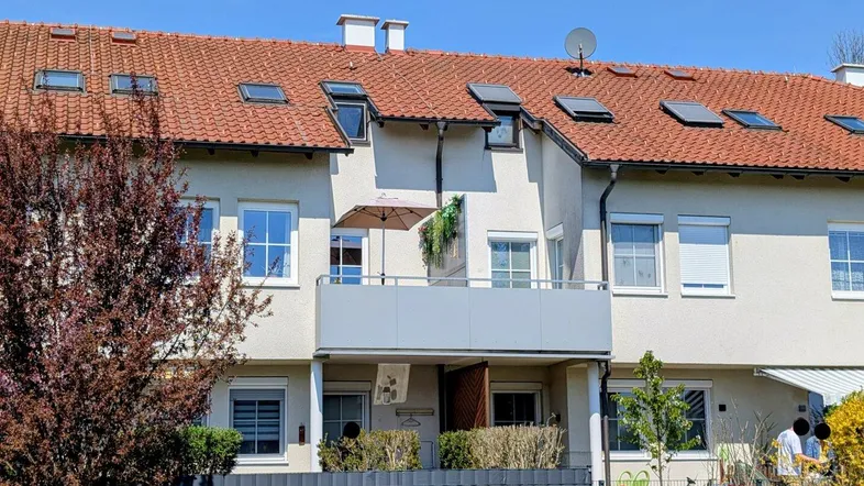 Fassade eines Reihenhauses mit Balkon und Dachfenstern unter blauem Himmel.