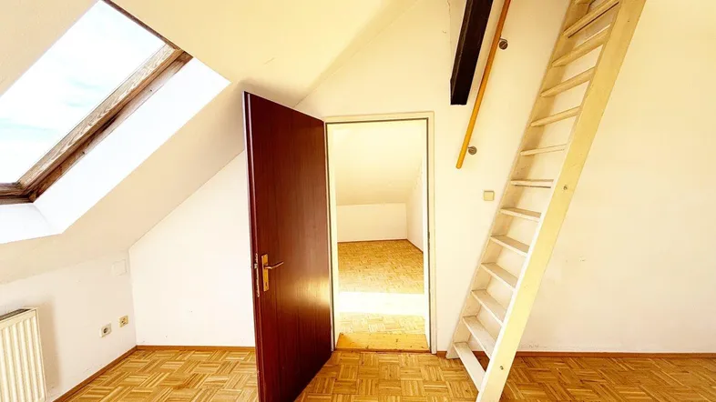 Helles Dachzimmer mit Parkettboden, Dachfenster und Zugang zu einem weiteren Raum über eine Leiter.