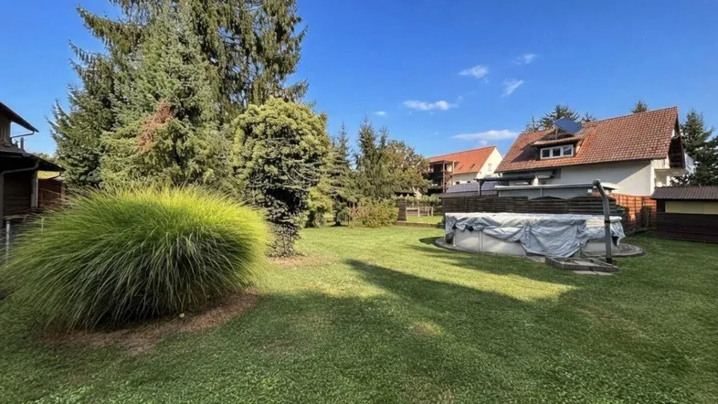 Großer Garten mit Rasenfläche, hohen Bäumen und einem abgedeckten Aufstellpool.