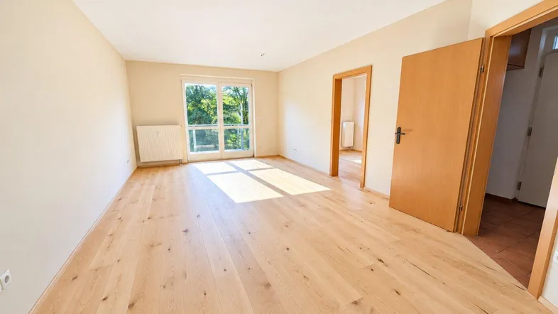Helles Wohnzimmer mit Holzboden und Zugang zum Balkon, durchflutet von natürlichem Licht.