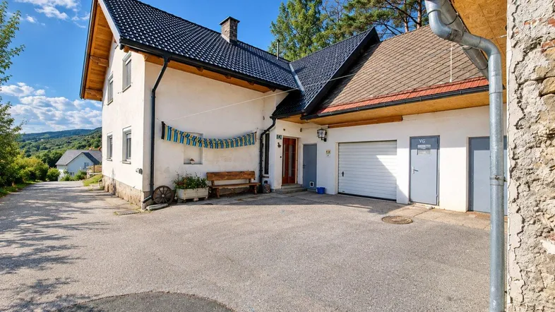 Weißes Haus mit dunklem Dach, Garage und gepflasterter Einfahrt in ländlicher Umgebung.