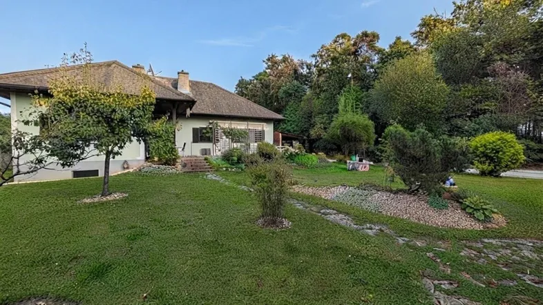 Großer, gepflegter Garten mit Rasenflächen, Sträuchern und einem charmanten Haus im Hintergrund.