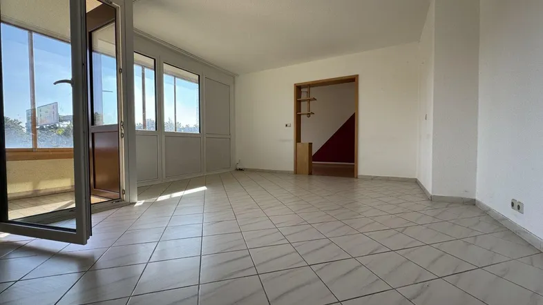 Helles Wohnzimmer mit Fliesenboden und Zugang zu einem verglasten Balkon, der viel Tageslicht bietet.