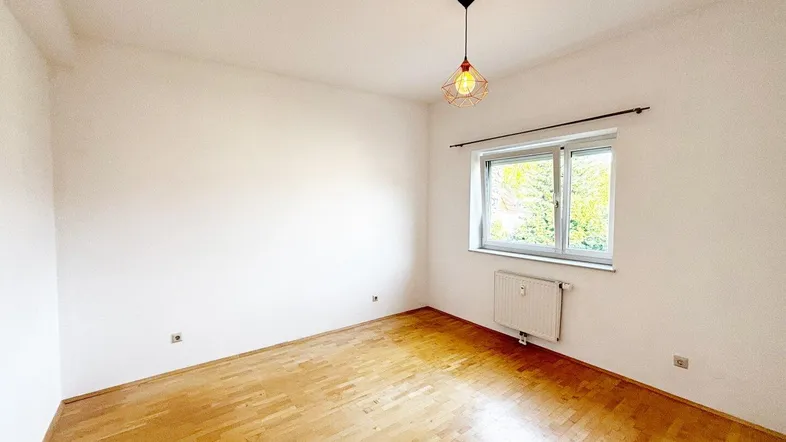 Helles Zimmer mit Parkettboden und Fenster, ideal als Schlaf- oder Arbeitszimmer.