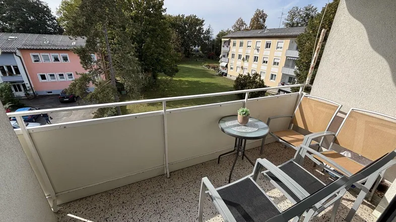 Möblierter Balkon mit Blick ins Grüne und auf umliegende Wohngebäude.