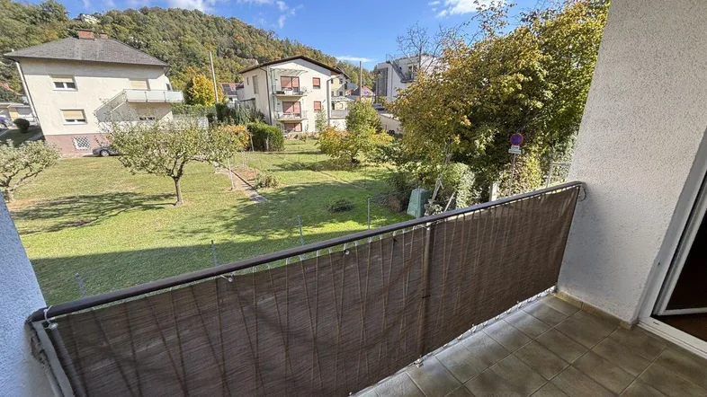 Balkon mit Blick auf den Garten, umliegende Häuser und grüne Hügel in der Ferne.