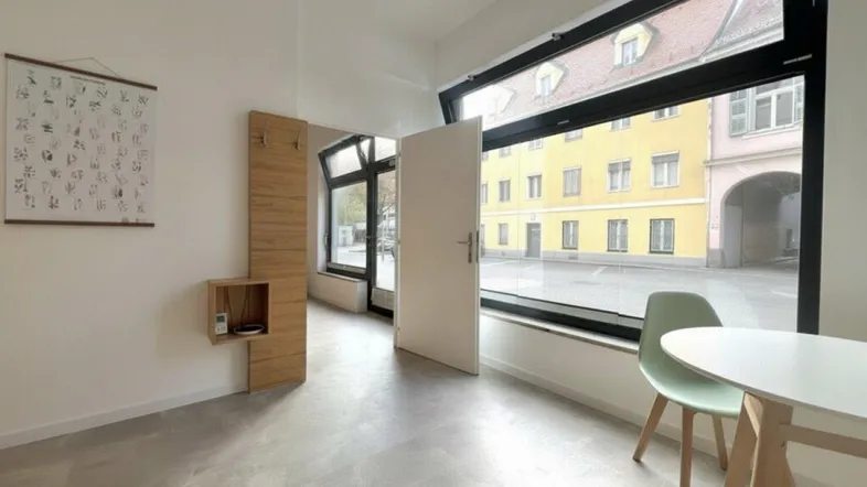 Heller Innenraum mit großen Fenstern, die einen Blick auf den Innenhof bieten, und modernem Mobiliar.