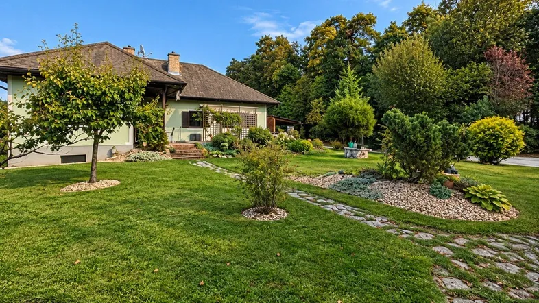 Haus mit gepflegtem Garten, Rasenflächen und Steinwegen unter blauem Himmel.