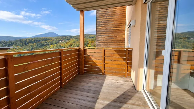 Geräumiger Balkon mit Holzboden und -geländer, bietet einen weiten Blick auf die umliegende Berglandschaft unter blauem Himmel.