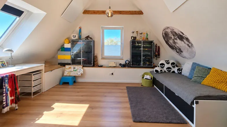 Helles Kinderzimmer im Dachgeschoss mit Holzbalken, Schreibtisch und Bett.