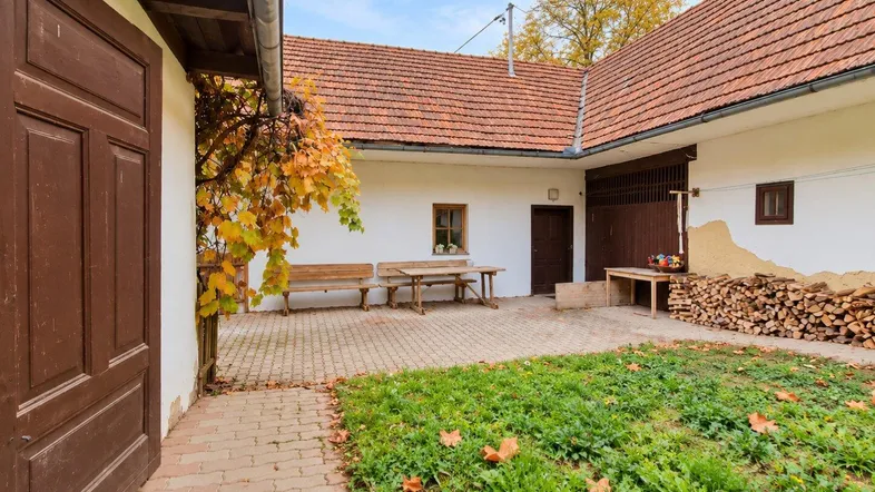 Traditioneller Innenhof mit Sitzgelegenheiten, Holzlager und herbstlicher Vegetation, umgeben von Gebäuden.