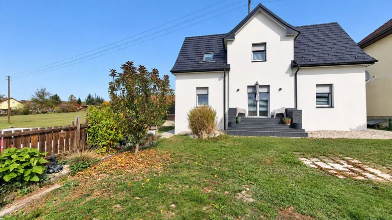 Modernes Einfamilienhaus mit weißer Fassade, dunklem Dach und einem gepflegten Gartenbereich.
