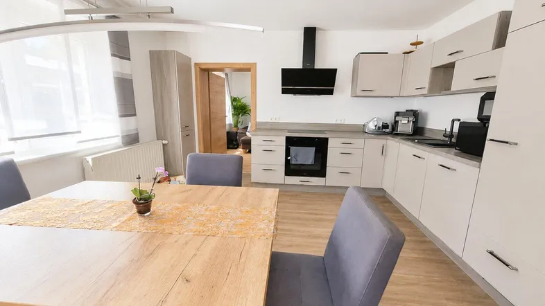 Moderne Küche mit hellen Schränken, integrierten Geräten und einem Essbereich mit Holztisch.