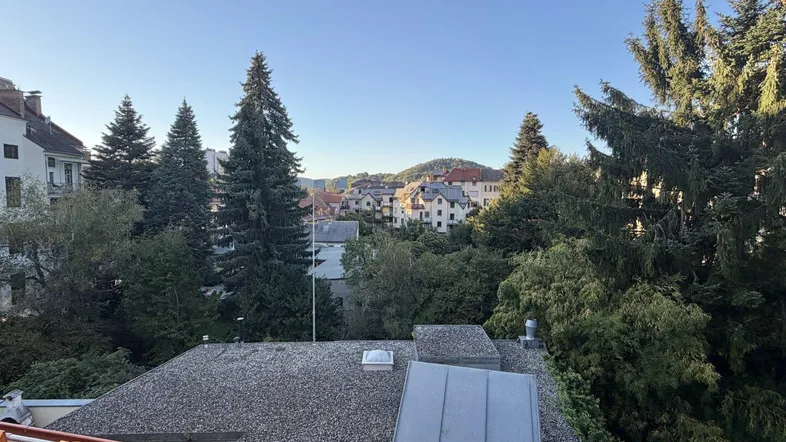 Weitblick über Dächer und grüne Hügel mit Wohngebäuden unter klarem Himmel.