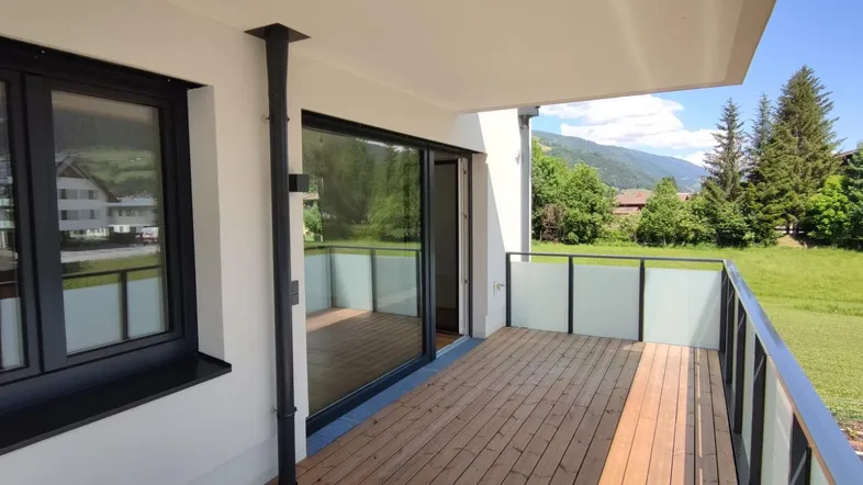 Geräumiger Balkon mit Holzboden, Glasgeländer und weitem Blick auf die umliegende Berglandschaft.