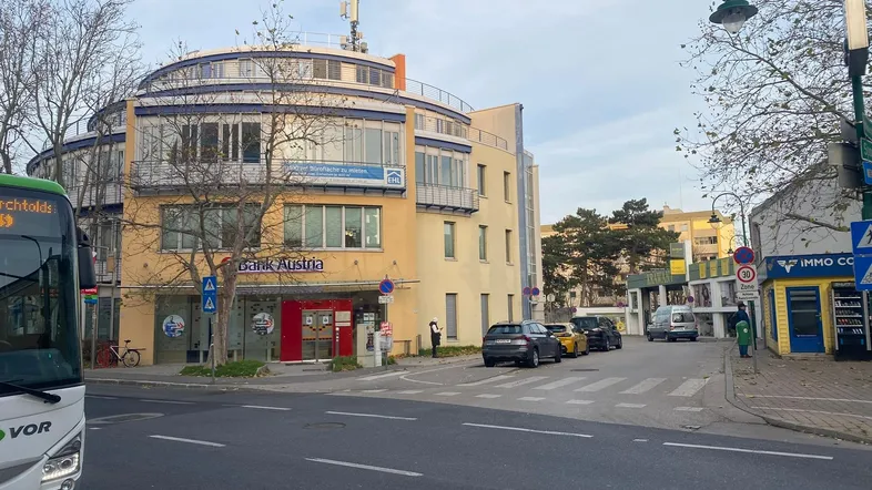 Gebäude mit runder Fassade an einer belebten Straße mit parkenden Autos und einem Bus.